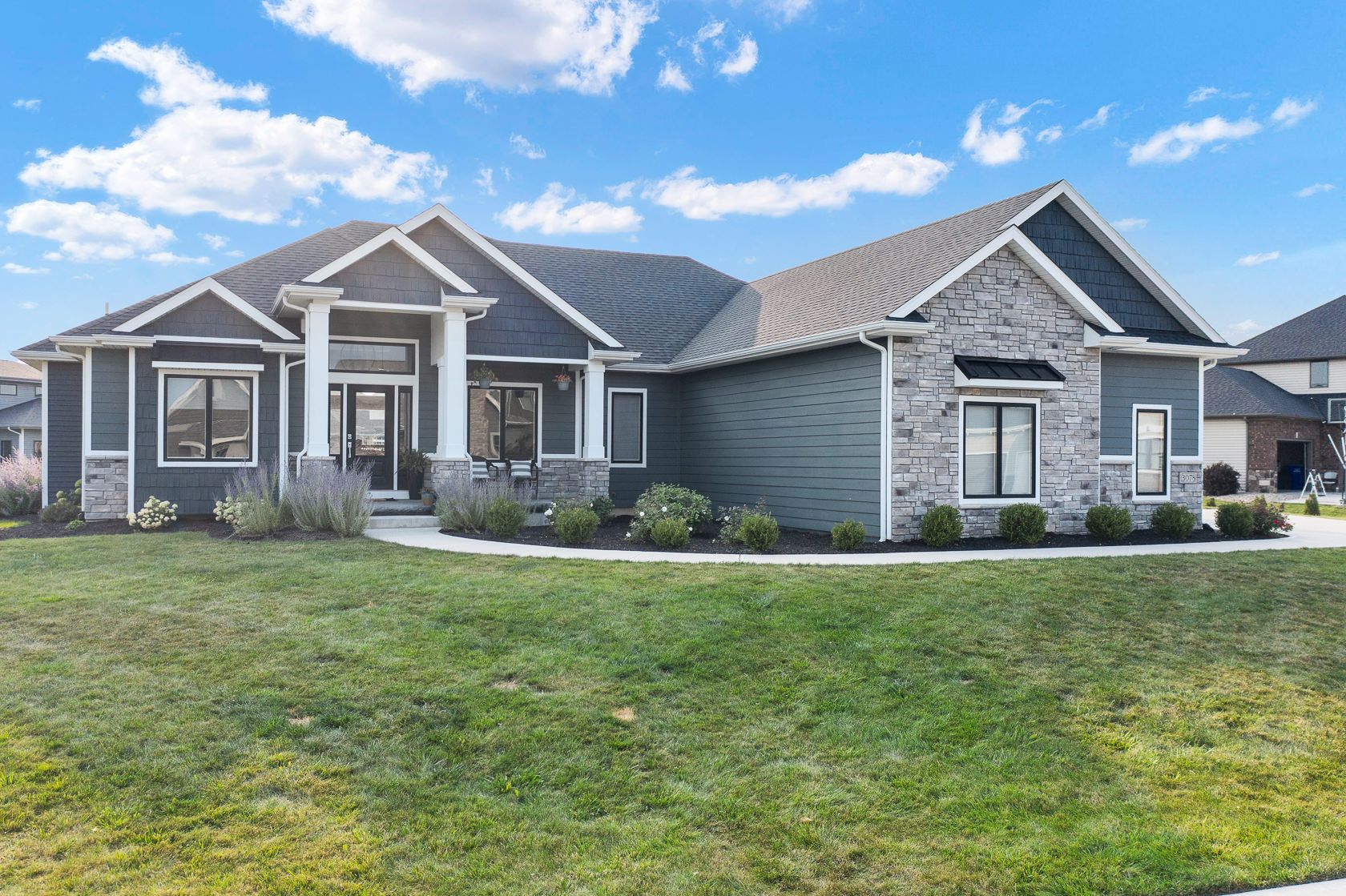 Front exterior of a completed single-storey home with stone and grey siding