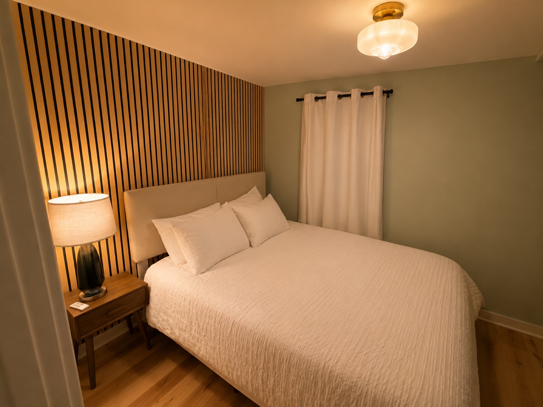 Bedroom with slatted wood accent wall, white linens, and a warm bedside lamp