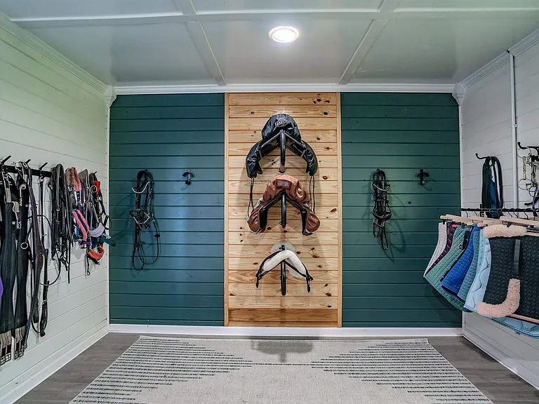 Tack room with saddles and bridles on a wood-slat wall